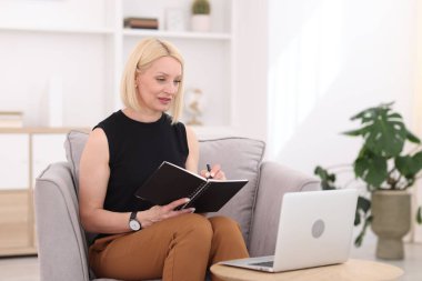 Ofiste dizüstü bilgisayarla çalışırken not alan profesyonel bir psikolog.