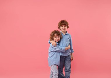 Pembe arka planda kucaklaşan sevimli küçük kardeşler.