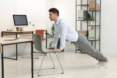 Ofiste sandalyeyle egzersiz yapan yakışıklı adam.