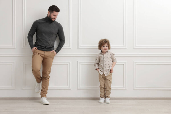Счастливый отец и его сын возле белой стены в помещении