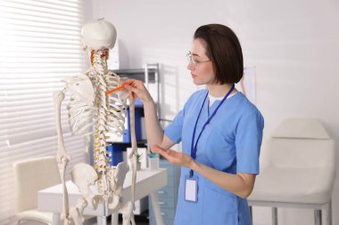 Doktor klinikteki insan iskeleti parçalarına işaret ediyor.