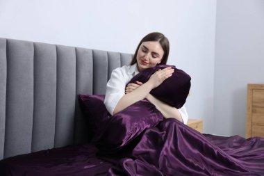 Mor ipek çarşaflarla yatakta yastığa sarılan bir kadın.