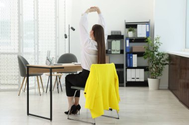 Genç bir kadın ofiste sandalyede uzanıyor.