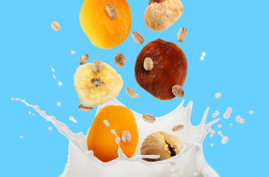 Süt sıçraması, yulaf ezmesi ve açık mavi arka planda kuru meyveler.