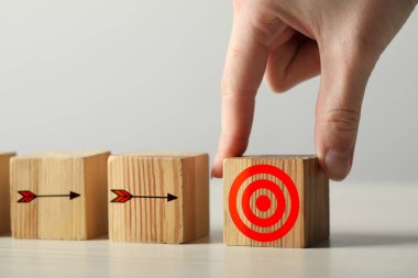 Hedef alınıyor. Masaya tahta küp koyan kadın, yakın plan. Oklu küplerin hedefi tam isabet.