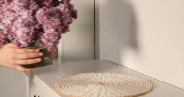 İçerideki dolabın üzerine güzel leylak çiçekleri yerleştiren kadın, yakın plan.