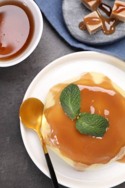 Delicious pudding with caramel sauce and mint served on gray textured table, flat lay