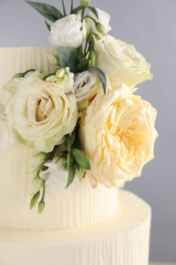 Gri arka planda çiçeklerle süslenmiş lezzetli düğün pastası, yakın plan.