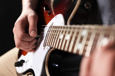 Siyah arkaplanda arabulucuyla gitar çalan adam, yakın plan