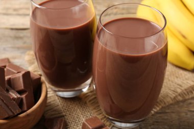 Lezzetli çikolatalı süt bardaklarda, parçalar ve muzlar ahşap masada, yakın plan