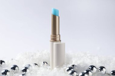 Nemlendirici dudak kremi ve yapay kar üzerindeki Noel süsü beyaz arka planda, yakın plan. Kış bakımı