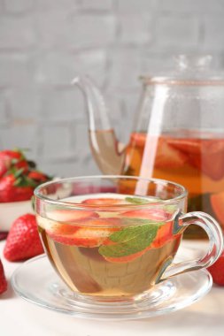 Aromatik meyve çayı, çilek ve nane şekeri beyaz masada, yakın plan.