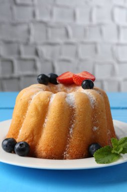 Açık mavi ahşap masa üzerinde pudra şekeri ve böğürtlenli Lezzetli kek, yakın plan. Metin için boşluk