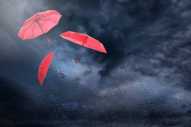 Koyu bulutlu gökyüzünde uçan kırmızı şemsiyeler, ıslak pencereden manzaralı. Fırtınalı hava