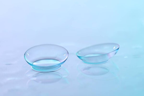 Pair of contact lenses and water drops on blue gradient mirror surface, closeup