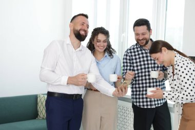 Ofisteki kahve molasında iş arkadaşlarına telefonunda bir şey gösteren bir adam.