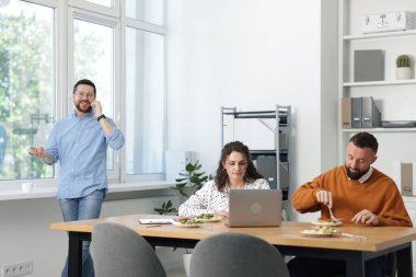 İş arkadaşları ofiste yemek yiyor ve sohbet ediyorlar.