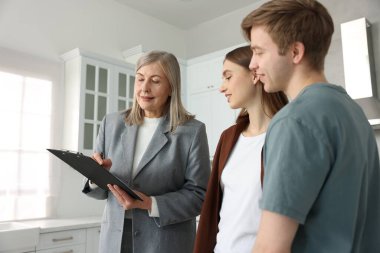 Dosyası olan bir emlakçı mutfakta bir çiftle çalışıyor.