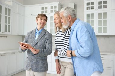 Mutfakta çiftlerle çalışan tabletli gülümseyen emlakçı.