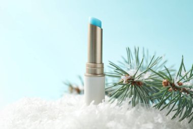 Nemlendirici dudak kremi ve yapay kar üzerindeki köknar ağacı dalları açık mavi arka planda, yakın plan. Kış bakımı