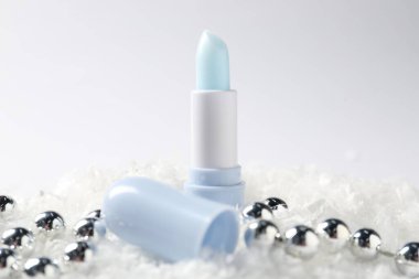 Nemlendirici dudak kremi ve yapay kar üzerindeki Noel süsü beyaz arka planda, yakın plan. Kış bakımı