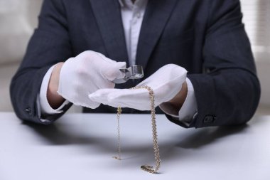 Beyaz masa içerisindeki lüks gerdanlığı değerlendiren eksper, yakın plan.