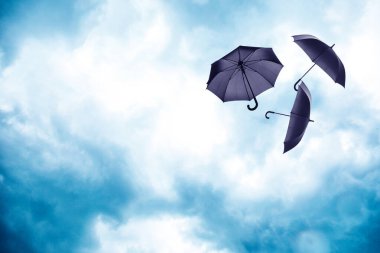 Bulutlu gökyüzünde uçan siyah şemsiyeler. Fırtınalı hava