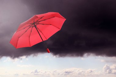 Bulutlu gökyüzünde uçan kırmızı şemsiye. Fırtınalı hava