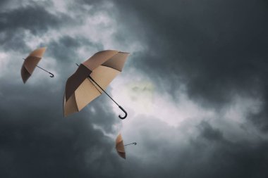 Koyu bulutlu gökyüzünde uçan kahverengi şemsiyeler. Fırtınalı hava