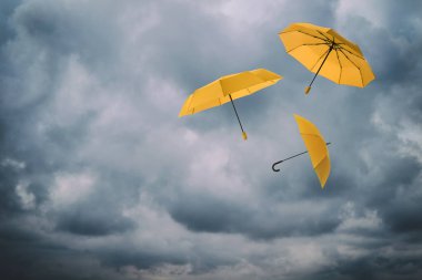 Bulutlu gökyüzünde uçan turuncu şemsiyeler. Fırtınalı hava