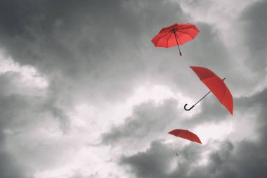 Bulutlu gökyüzünde uçan kırmızı şemsiyeler. Fırtınalı hava
