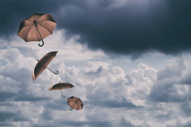 Bulutlu gökyüzünde uçuşan kahverengi şemsiyeler. Fırtınalı hava