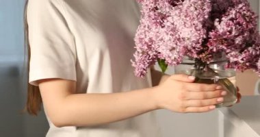 İçerideki dolabın üzerine güzel leylak çiçekleri yerleştiren kadın, yakın plan.