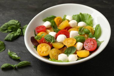 Sarı domatesli lezzetli salata, fesleğen ve siyah masada mozzarella peyniri, yakın plan.