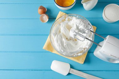 Açık mavi ahşap masada çırpılmış krema ve çırpılmış çırpılmış çırpılmış çırpılmış çırpma makinesi. Metin için boşluk