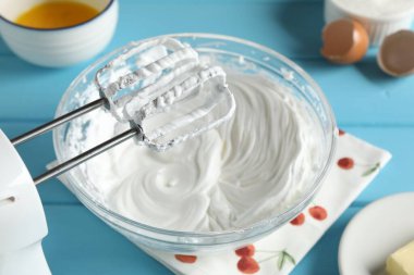 Açık mavi masada çırpılmış krema ve çırpılmış çırpılmış çırpılmış çırpıcı, yakın plan.