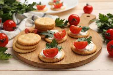 Krem peynirli krakerler, domatesler ve maydanozlar beyaz ahşap masada, yakın plan.