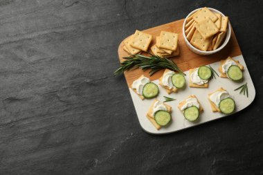 Krem peynirli krakerler, biberiye ve salatalık, koyu dokulu masa, üst manzara. Metin için boşluk