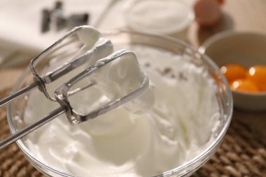 Masada çırpılmış krema ve çırpılmış kremayla el çırpıcı, yakın plan.