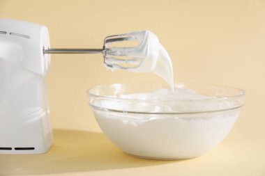 Bej arka planda çırpılmış krema ve çırpılmış kremayla el çırpıcı, yakın plan.