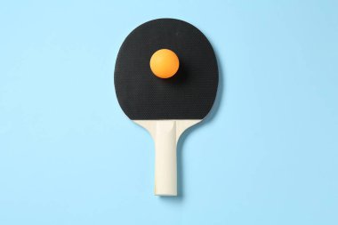 Açık mavi zemin üzerinde pinpon raketi ve top, üst görünüm