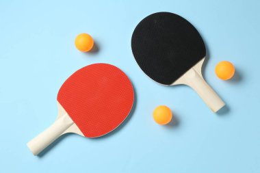 Masa tenisi raketleri ve topları açık mavi arka planda, düz yatıyordu.