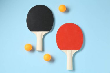 Masa tenisi raketleri ve topları açık mavi arka planda, düz yatıyordu.
