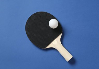 Mavi zemin üzerinde pinpon raketi ve top, üst görünüm
