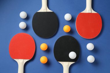 Masa tenisi raketleri ve topları mavi arka planda, düz yatıyordu.