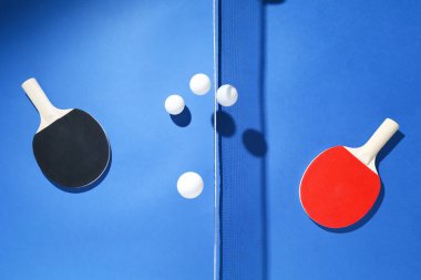 Masa tenisi raketleri, toplar ve ağ mavi arka planda, düz yatıyordu.