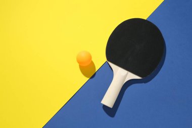 Renkli arka planda pinpon raketi ve top, üst görünüm. Metin için boşluk