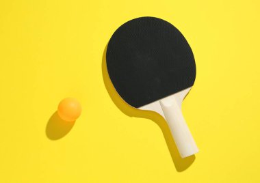 Sarı arka planda pinpon raketi ve top, üst manzara.