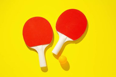 Masa tenisi raketleri ve top sarı arka planda, üst görünümde.