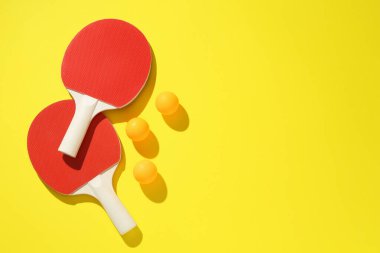 Masa tenisi raketleri ve toplar sarı arka planda, düz yerde. Metin için boşluk